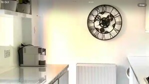 Una cocina moderna con encimera blanca, cafetera, reloj en la pared y radiador blanco.