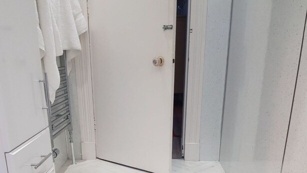 Una escalera conduce a una habitación con una puerta blanca, un perchero y un suelo de baldosas.