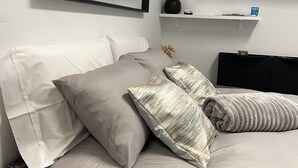 Una cama bien hecha con una colcha estampada, un espejo grande encima y una mesita de noche con un jarrón y un libro.