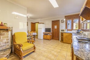 A spacious living area with a fireplace, a yellow armchair, a dining table, and a kitchen with a sink and stove.