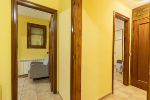 A hallway with a radiator, a chair, and a door leading to a room with a window and a radiator.