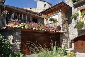 Un edificio in pietra dal caratteristico aspetto, con una porta in legno, balconi fioriti e cielo sereno.