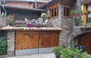 A stone building with a wooden door, a balcony with chairs, and potted plants.