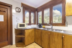 A kitchen with wooden cabinets, a microwave, a sink, and a window with a view of the outdoors. - Apartment 1 | Casa Teulé | Sleeps 5 + 2 (Les Iglésies)