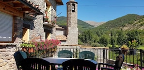 Un edificio in pietra con un campanile, posti a sedere all'aperto e vista su un paesaggio montuoso.