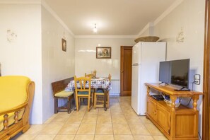 A compact kitchen with a dining table, chairs, a refrigerator, and a television on a wooden stand.