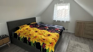 A bedroom with a bed, a nightstand, a dresser, a window with curtains, and a radiator. - Vacation apartments near Legoland-Günzburg (Günzburg)