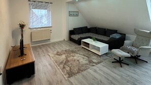 A modern living room with a sectional sofa, a white coffee table, a grey accent chair, and a small side table with a vase. - Vacation apartments near Legoland-Günzburg (Günzburg)