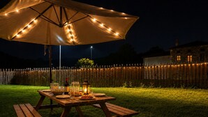 Ein Holztisch mit Picknickdecke und Lichterkette, platziert auf einer Rasenfläche bei Nacht.