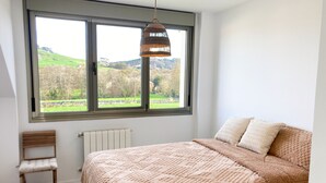 Ein Schlafzimmer mit einem großen Fenster, einem Bett mit gemustertem Überwurf, einem Holzstuhl und einer Heizung.