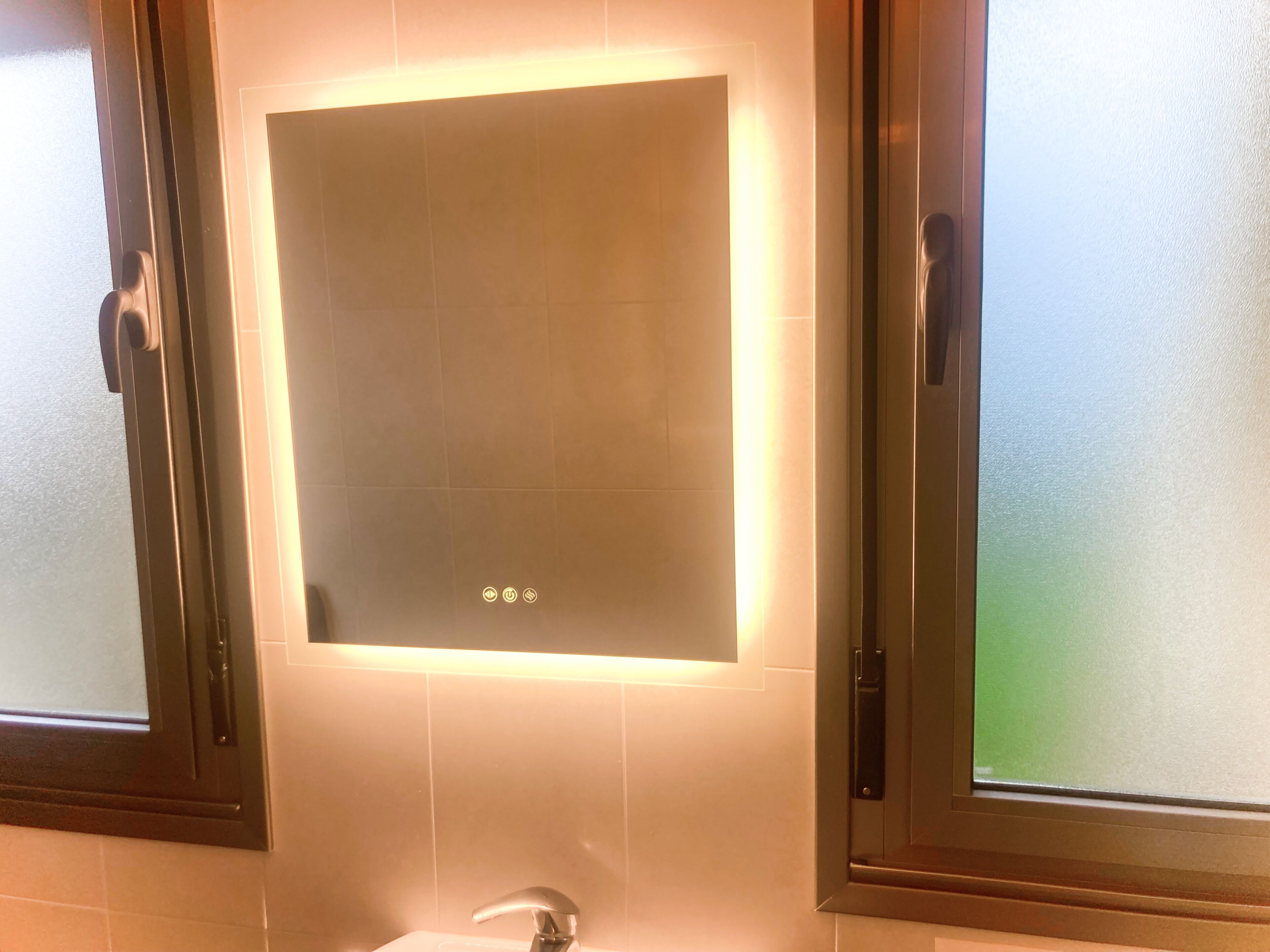 Une salle de bain dotée d’un meuble-lavabo moderne, d’un miroir aux bords éclairés et d’une fenêtre en verre dépoli.