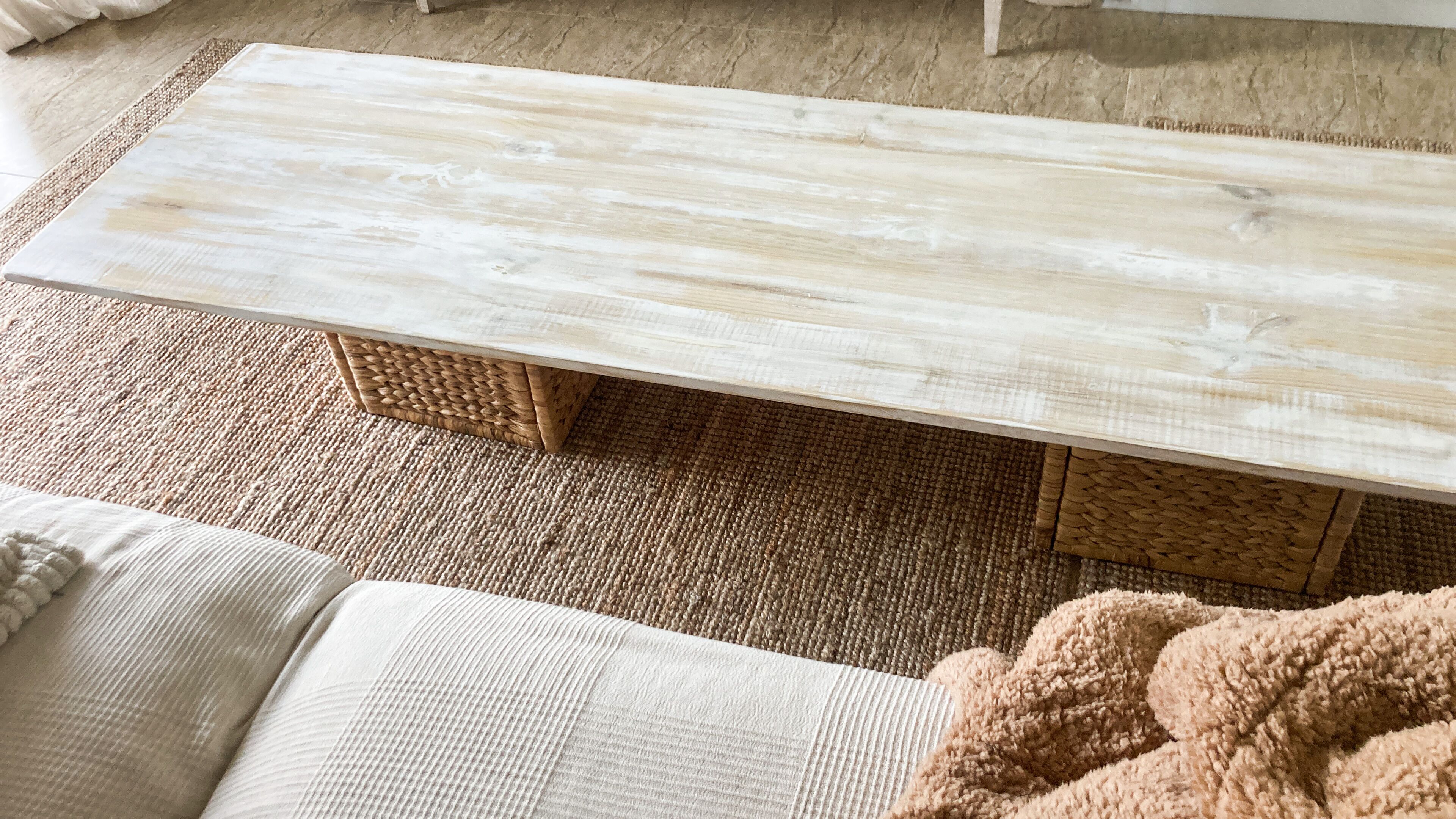 A wooden coffee table with woven baskets underneath, placed on a textured rug.