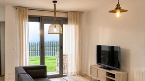 Ein modernes Wohnzimmer mit einem Ecksofa, einem Flachbildfernseher und einem großen Fenster mit Blick auf eine Rasenfläche.