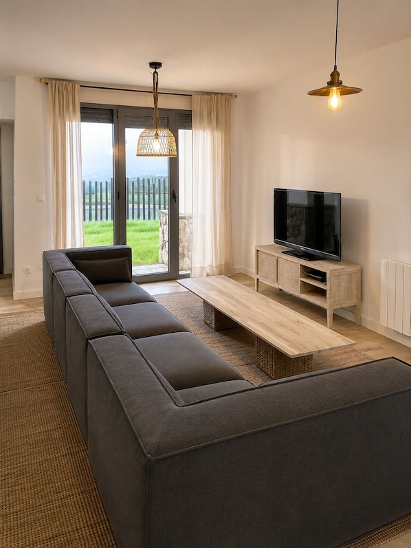 A modern living room with a sectional sofa, a flat-screen TV, and a large window with a view of a grassy area.