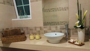 A bathroom with a large white sink, a glass shower enclosure, a small window with bottles, a wicker basket, and a vase with flowers. - Quinta da Queiró (Ponta Delgada)