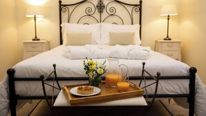 A neatly made bed with white linens, two bedside lamps, a tray with breakfast items, and a vase of flowers.