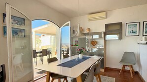Un coin repas comprenant une table, des chaises, un vase avec des fleurs et une vue sur l’extérieur, visible à travers une porte ouverte.
