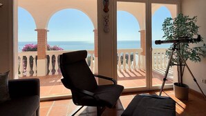 Une pièce avec un balcon, une chaise, un télescope et une plante en pot.