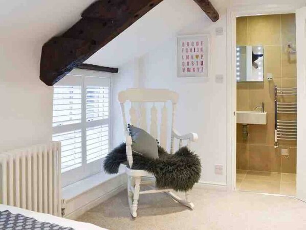A room with a white rocking chair, a radiator, a window with blinds, a bathroom with a towel rack, and a wall-mounted mirror. - Cosy and characterful cottage in the heart of Kirkby Lonsdale (Kirkby Lonsdale)