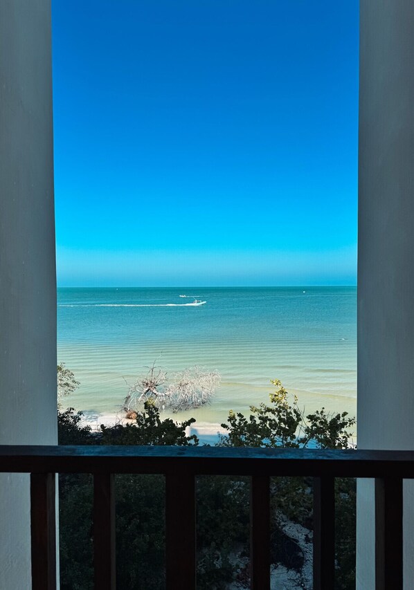 A view from a balcony overlooking a beach with calm waters and a clear sky.