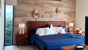 A modern bedroom with a large bed, wooden headboard, two bedside tables with lamps, a wooden nightstand, and a small table with a basket. - Chic Loft Steps from the Jungle View (Holbox)