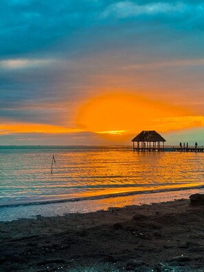A beach with a wooden pier and a thatched-roof structure.