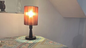 A room with a table covered by a patterned tablecloth, a lamp with a cylindrical shade, and a wooden chair with a curved backrest. - Swarnapaya résidence (Bentota)