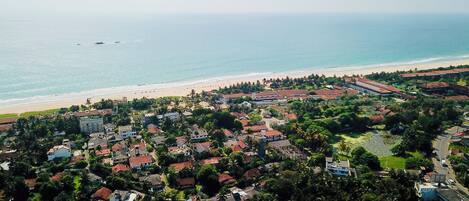 An aerial view of a coastal town with residential buildings, a beach, and a large open area with a road.