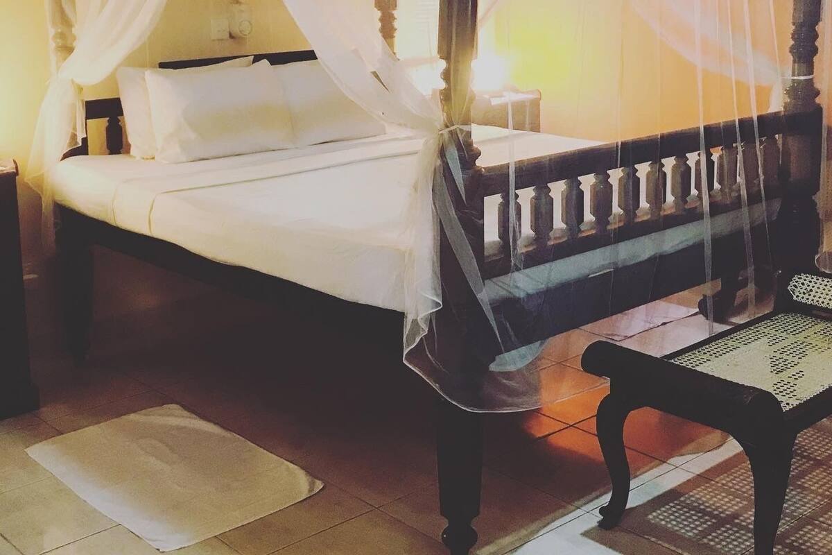 A bed with a canopy, a nightstand, a chair, and a wall with a patterned design.