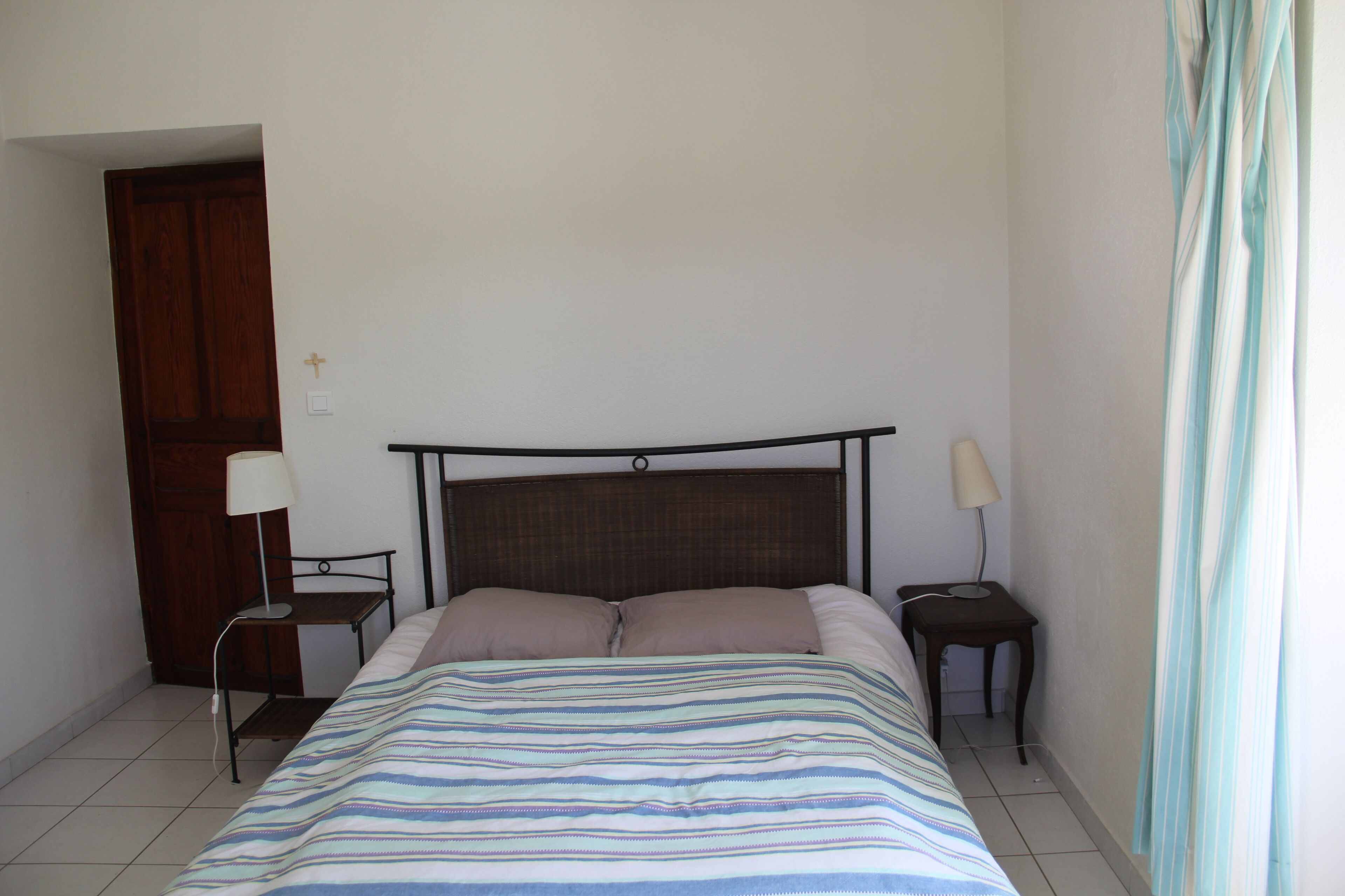 A bedroom with a bed, two bedside tables, a nightstand, a wooden door, and a curtain.