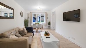 Un saló modern amb un sofà beix, una taula de centre blanca i una televisió penjada a la paret.