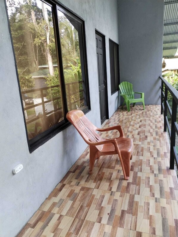 A balcony with a wooden floor, a wooden chair, and a green chair.