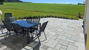 Un patio al aire libre con una mesa y sillas, vista a un campo verde y cielo despejado.