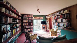 Una biblioteca con estanterías a ambos lados, un televisor sobre un soporte y una ventana con cortinas.
