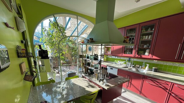 Una cocina con un ventanal grande, paredes verdes y armarios rojos.