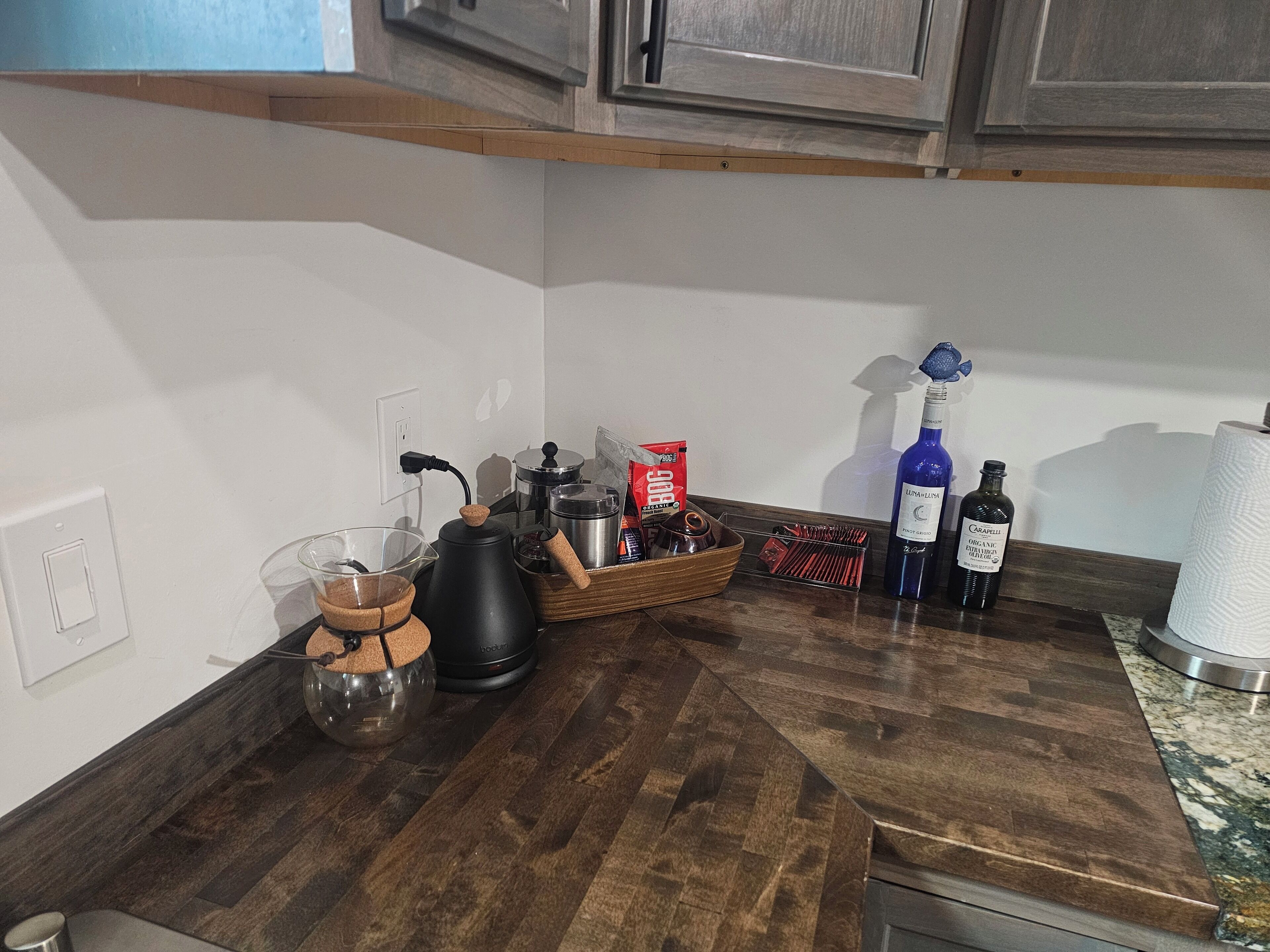 Een aanrecht met een koffiezetapparaat, een waterkoker, een fles wijn en een doosje theezakjes.