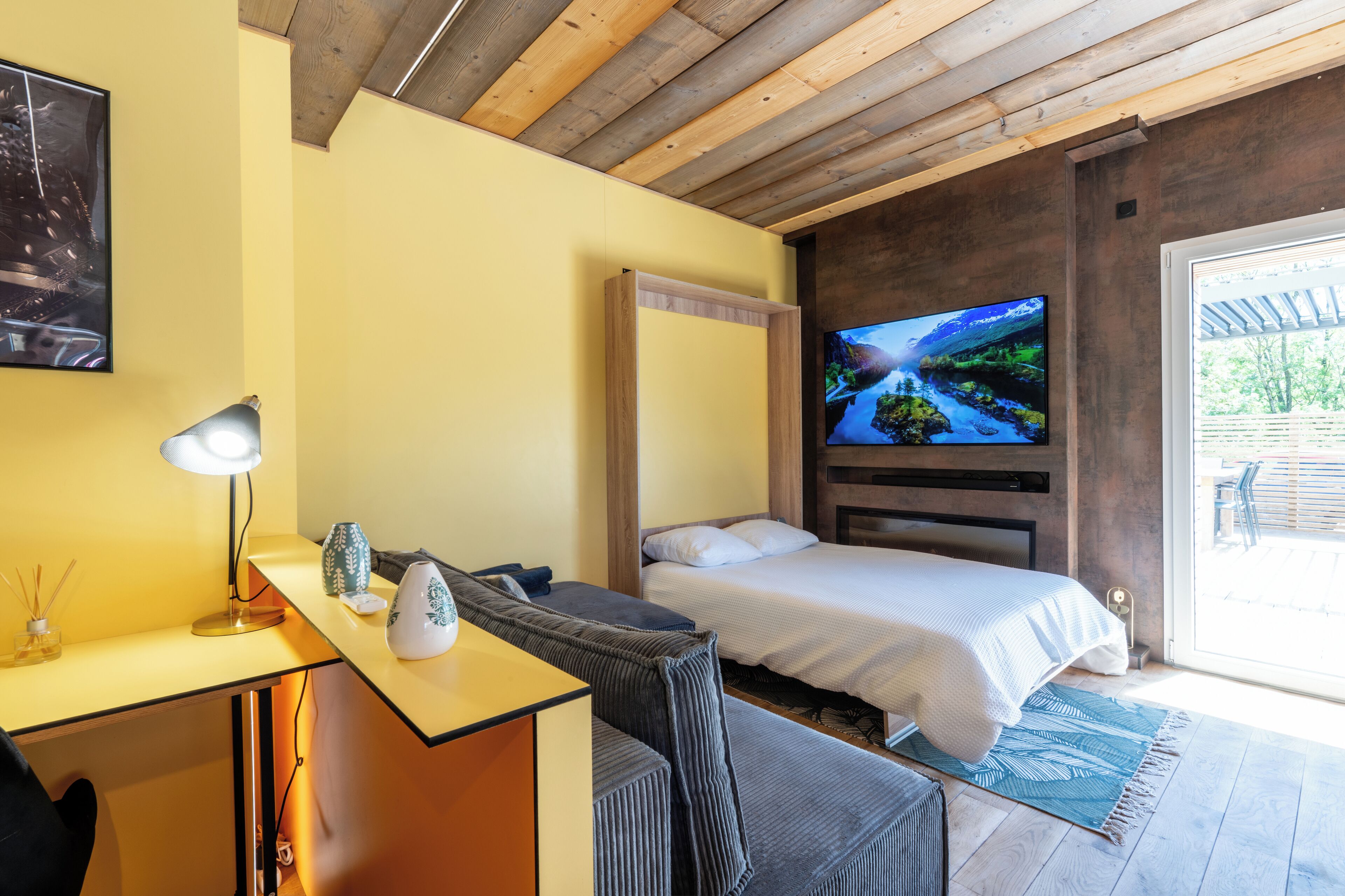 Een slaapkamer met een bed, een bureau met een lamp, een televisie en uitzicht op de omgeving.