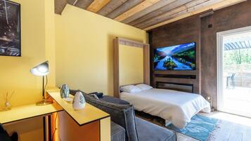 Een slaapkamer met een bed, een bureau met een lamp, een televisie en uitzicht op de omgeving.