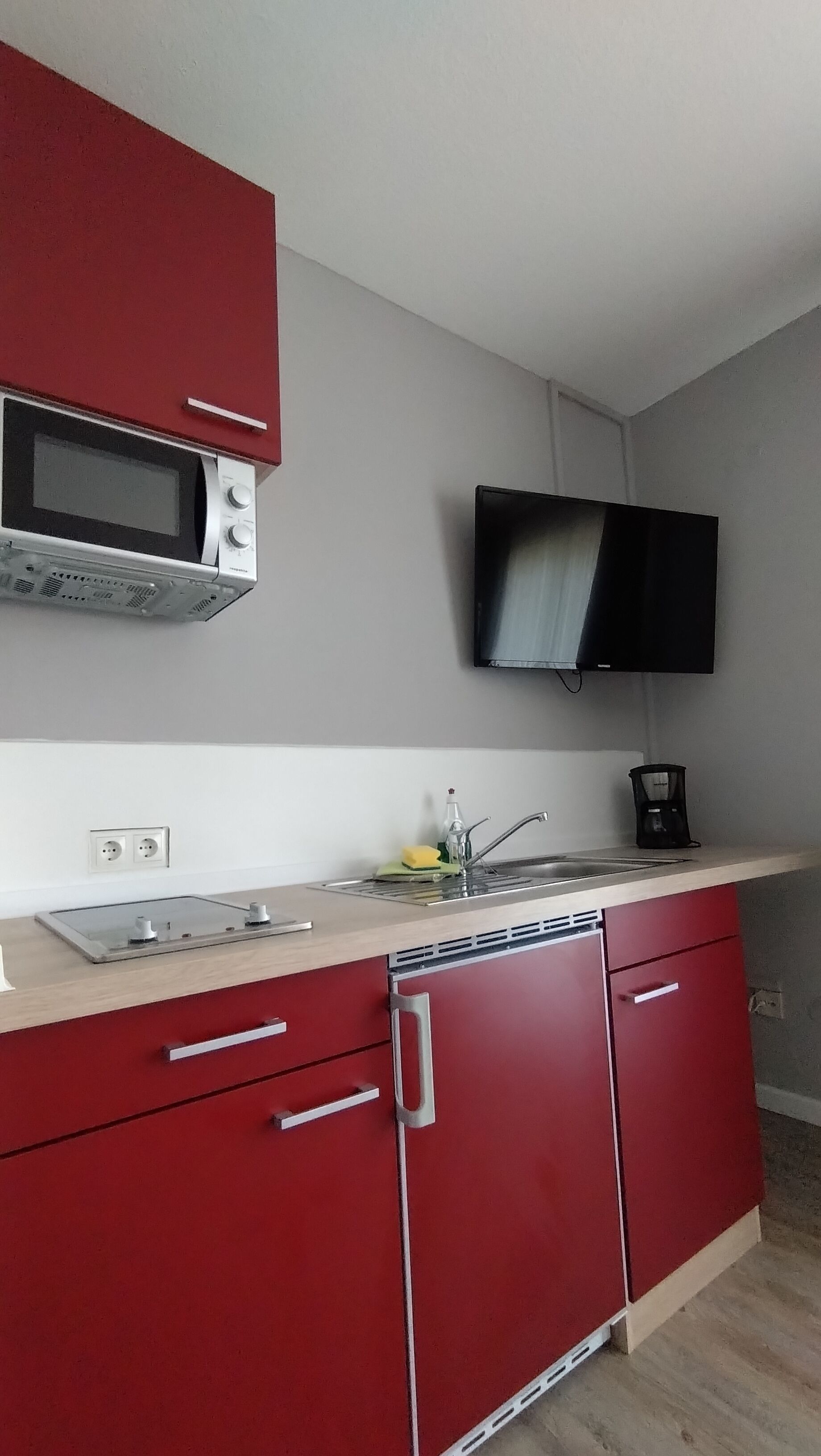 Uma cozinha compacta com micro-ondas, pia e cafeteira.