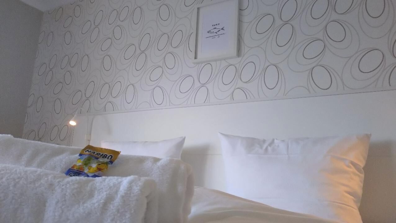A hotel room with a patterned wallpaper, a framed picture on the wall, and a bed with white linens.