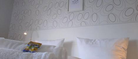 A hotel room with a patterned wallpaper, a framed picture on the wall, and a bed with white linens.