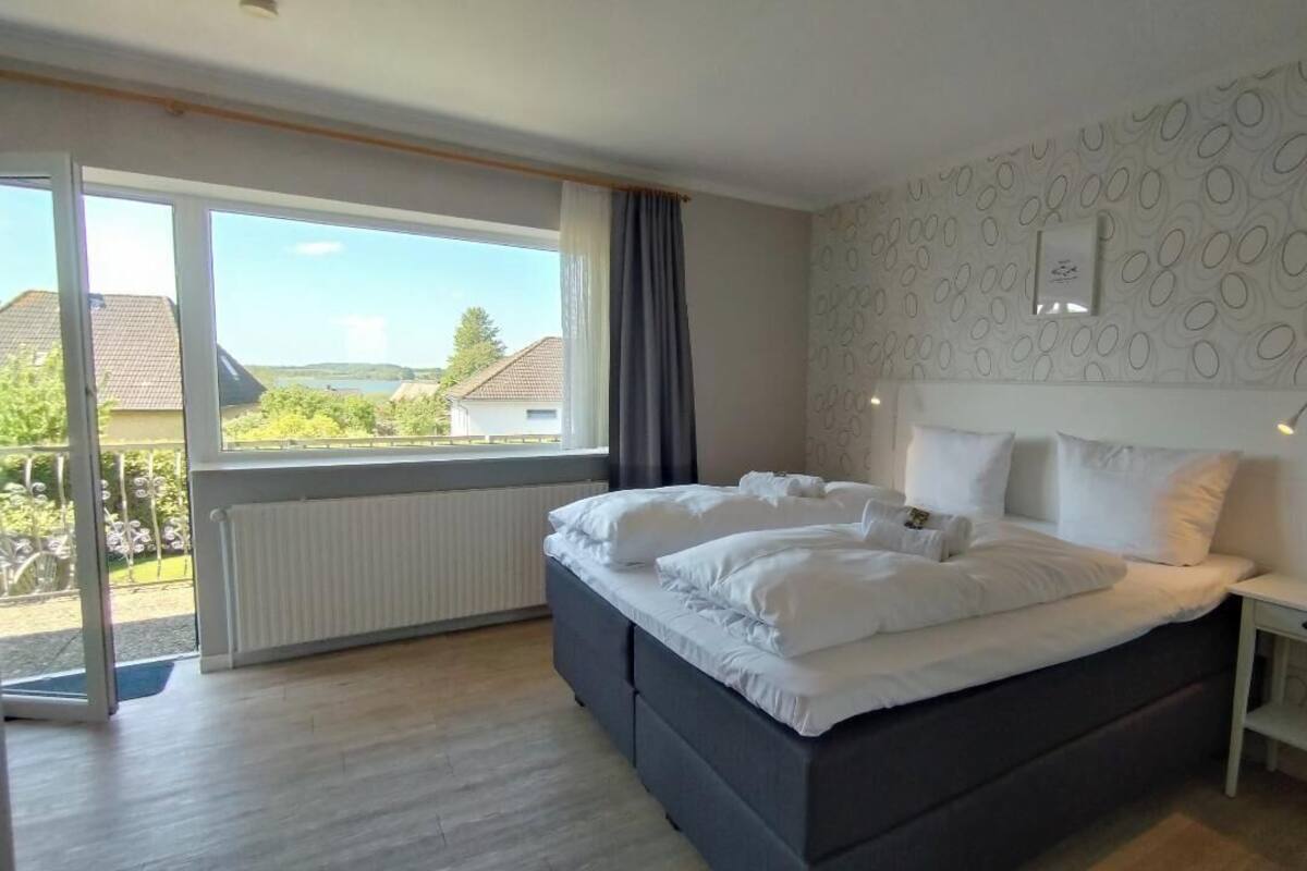 Een slaapkamer met een groot bed, een nachtkastje, een raam met gordijnen en uitzicht op de omgeving.