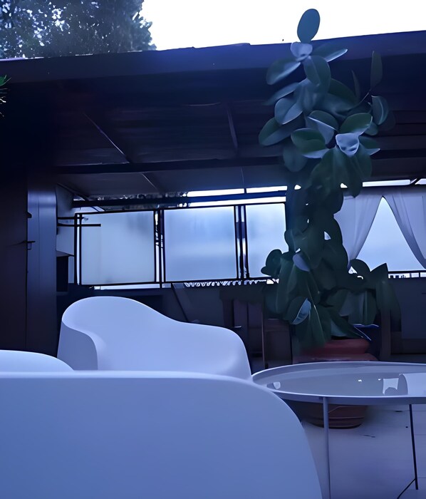 A modern outdoor seating area with white chairs and a table, surrounded by potted plants and a covered structure.