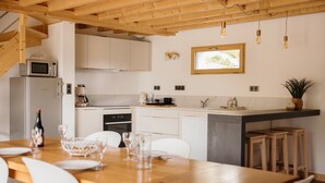 A modern kitchen with white cabinets, a wooden dining table, and bar stools.