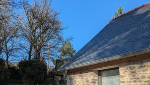A stone house with a sloped roof, a window, and a garden with mulch and plants.