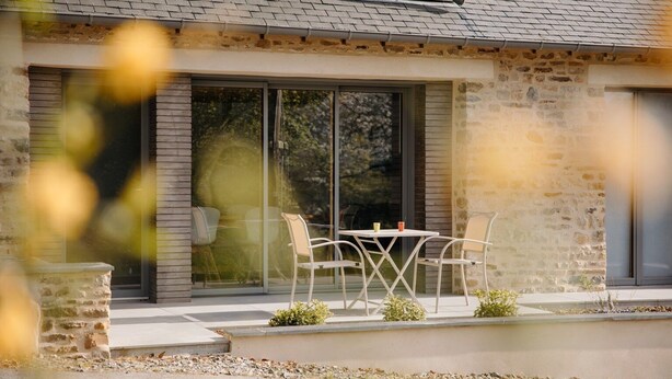 A modern house with a stone facade, large sliding glass doors, and a patio with a table and chairs.