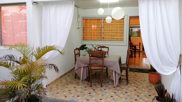 A dining area with a table set for four, surrounded by chairs, under white curtains. - Creole vacation home 15 minutes from the beach and 5 minutes from downtown! (Rivière-Salée)