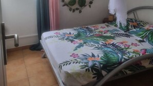 A room with a bed, a mosquito net, a window with curtains, a wall-mounted air conditioner, and a fan. - Creole vacation home 15 minutes from the beach and 5 minutes from downtown! (Rivière-Salée)