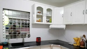 A kitchen with white cabinets, a black countertop, a window with a metal grill, and a red appliance. - Creole vacation home 15 minutes from the beach and 5 minutes from downtown! (Rivière-Salée)