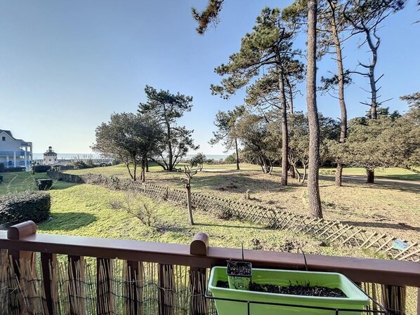 En balkon med udsigt over en anlagt have, med træer og et hegn.